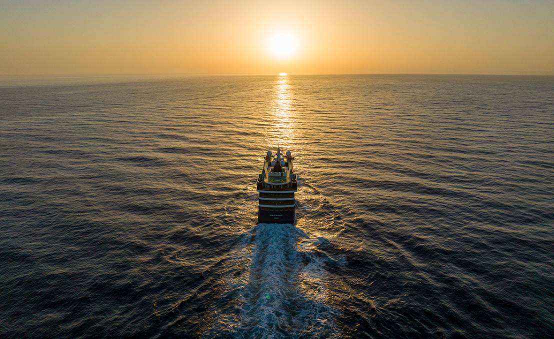 Barco navegando en el océano al atardecer con reflejo dorado en el agua