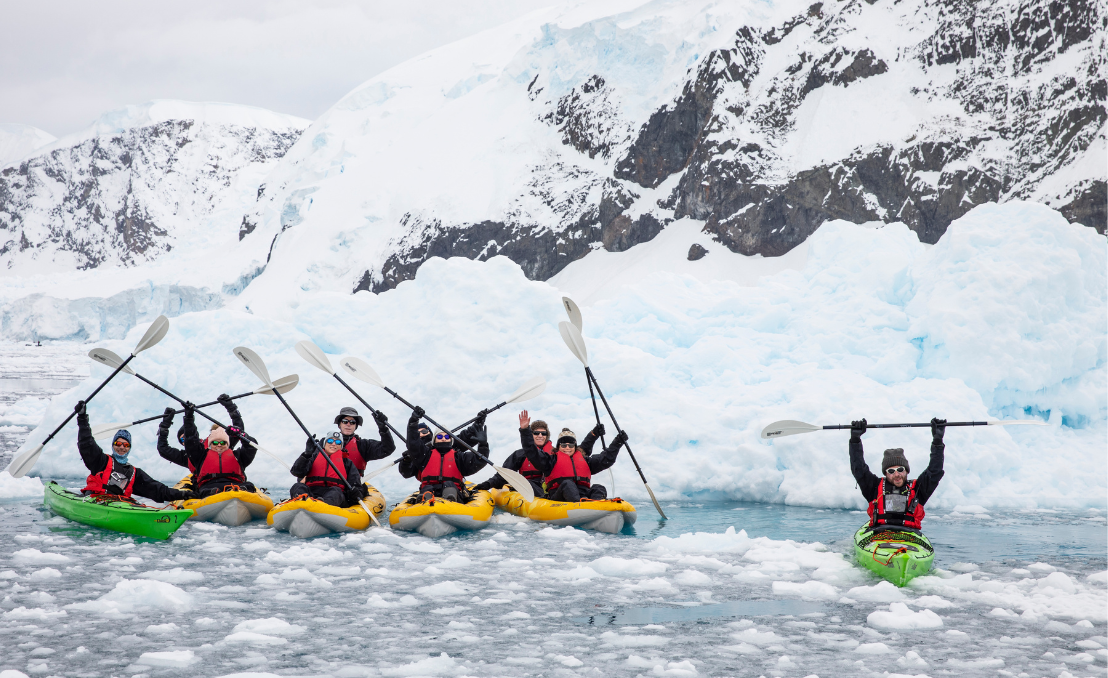 Grupo de pasajeros en kayaks en aguas polares rodeados de hielo y montañas nevadas
